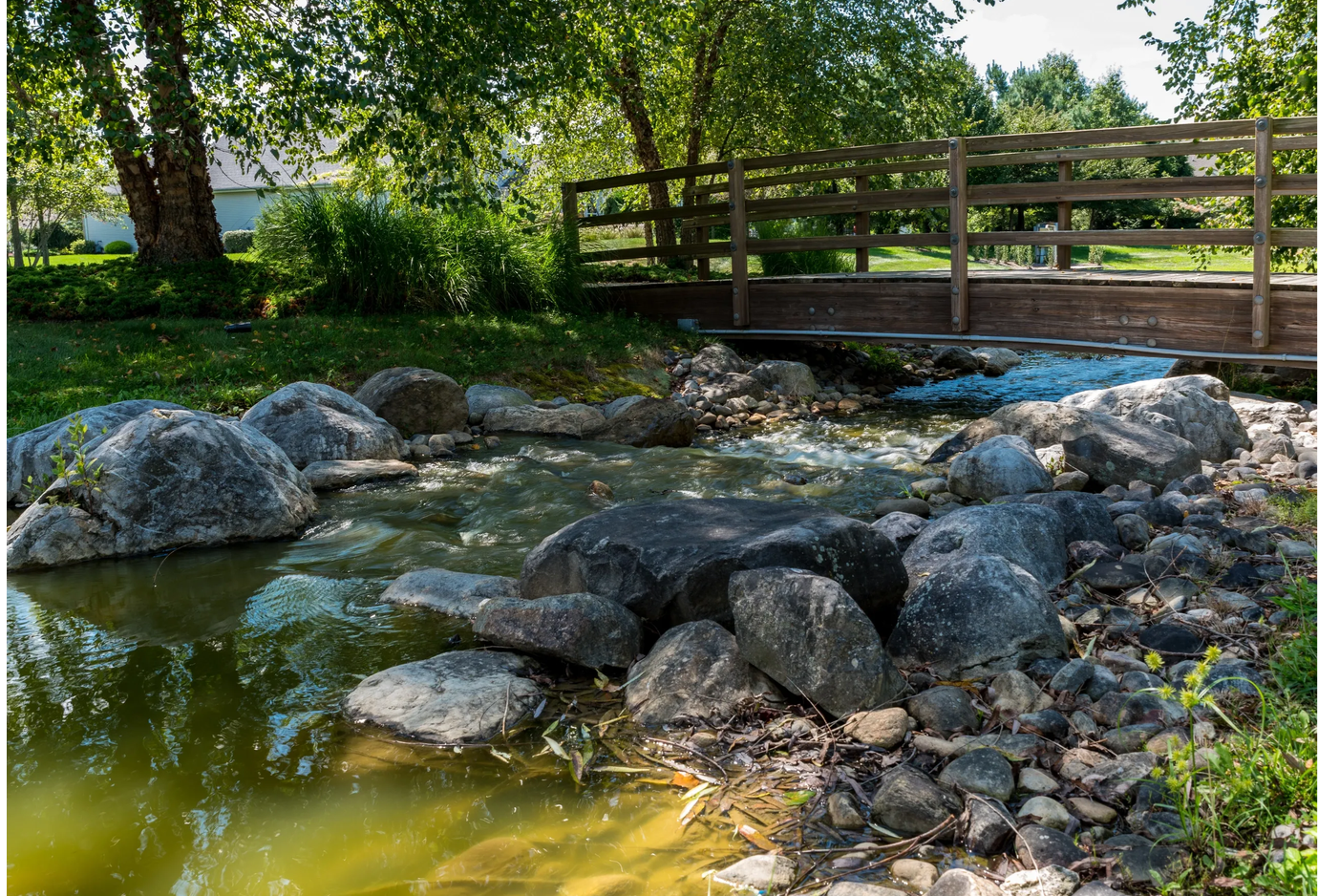 Scenic brook with wooden bridge and lush greenery at Four Seasons at Metedeconk Lakes